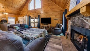 A cozy log cabin interior with a fireplace, a large bed, a sofa, and a television. - NEW! Updated Family Log Cabin+Hot Tub+Pool Table! (Sevierville)