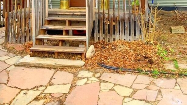Una casa con un porche delantero, una puerta marrón y un pequeño jardín con plantas y mantillo.