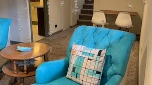 Un salón con un sillón azul verdoso, una mesita de madera y un reloj decorativo en la pared.