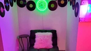 Una habitación con una cama, una mesita pequeña y una pared decorada con discos de vinilo y un reloj de neón.