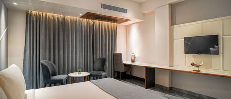 A hotel room with a large bed, two chairs, a small table, a desk, a television, and a curtain.