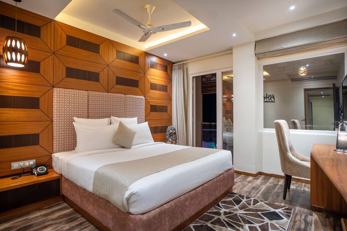A hotel room with a large bed, a ceiling fan, a desk with a chair, and a bathroom visible through an open door.