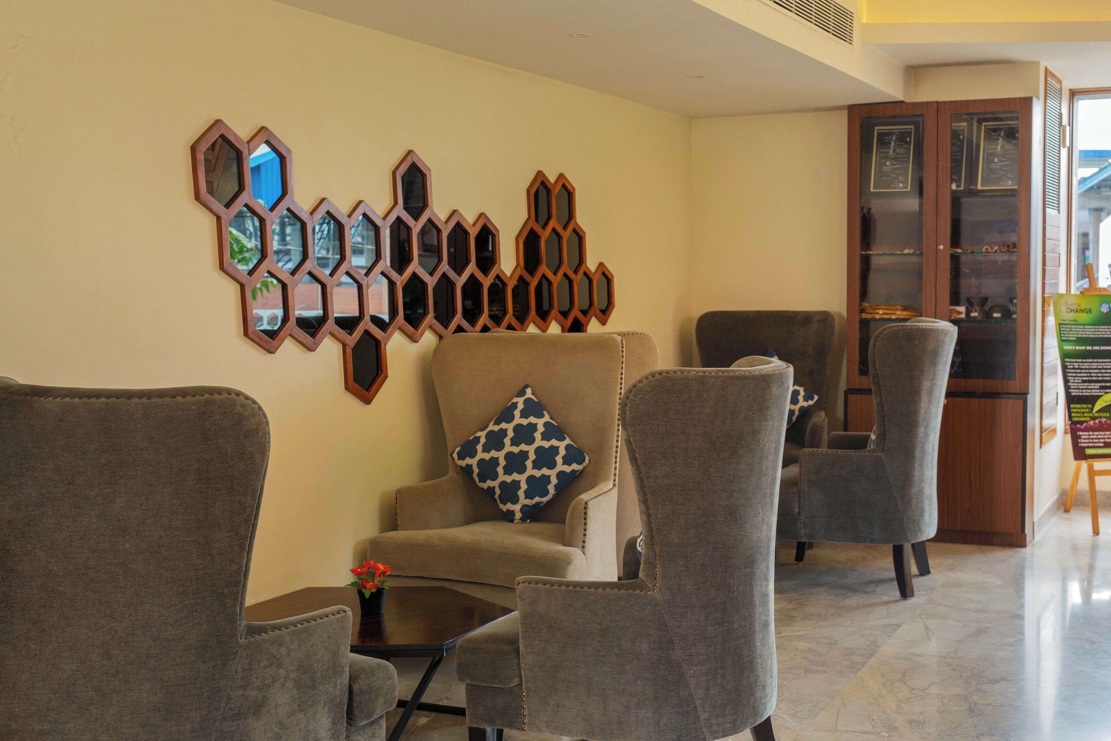 A lobby with a seating area featuring three armchairs, a sofa, and a wall-mounted mirror display.