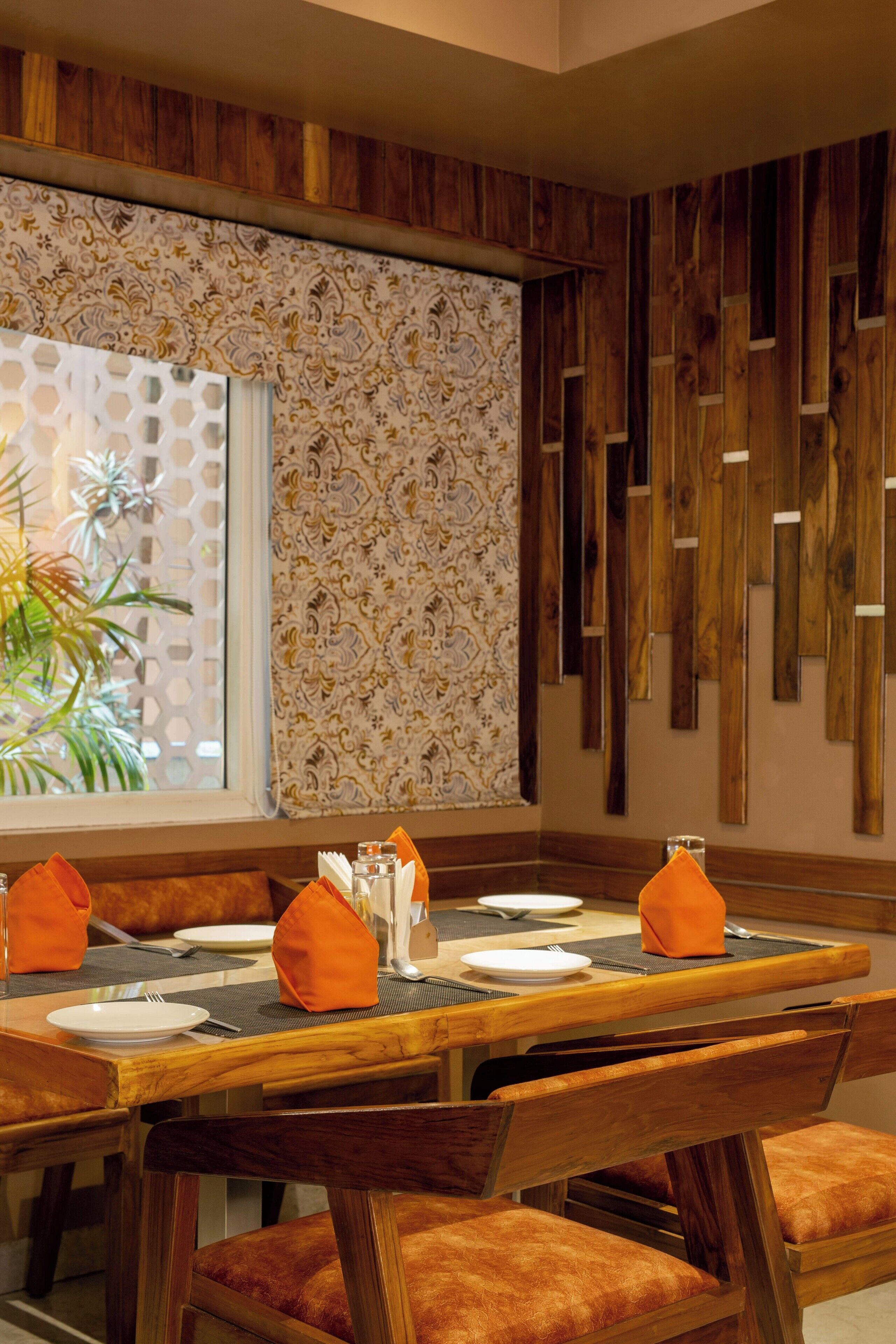 Comedor con mesa de madera dispuesta para cuatro, con servilletas anaranjadas y un florero.