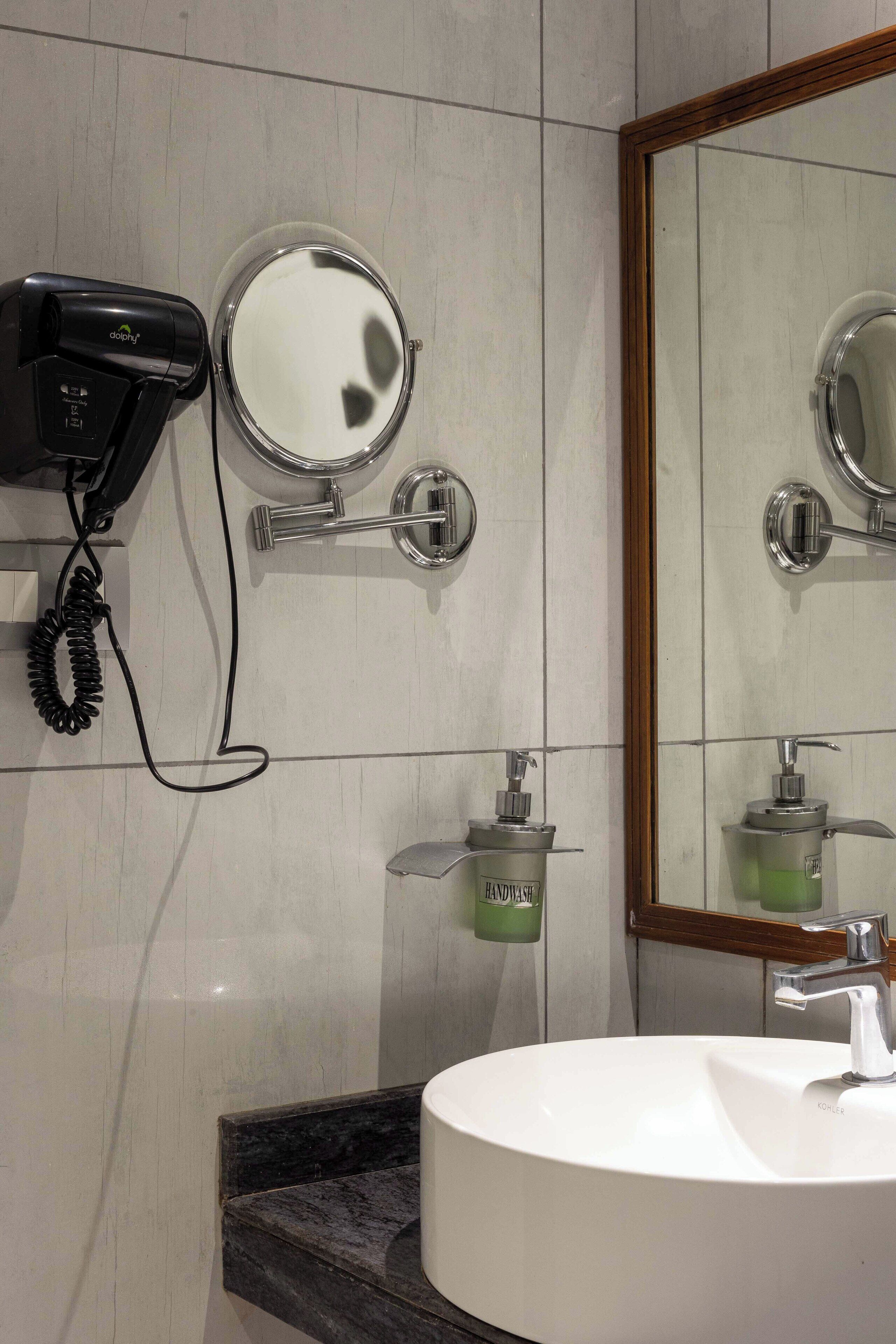 A bathroom with a round mirror, a hairdryer, a towel rack, and a sink.