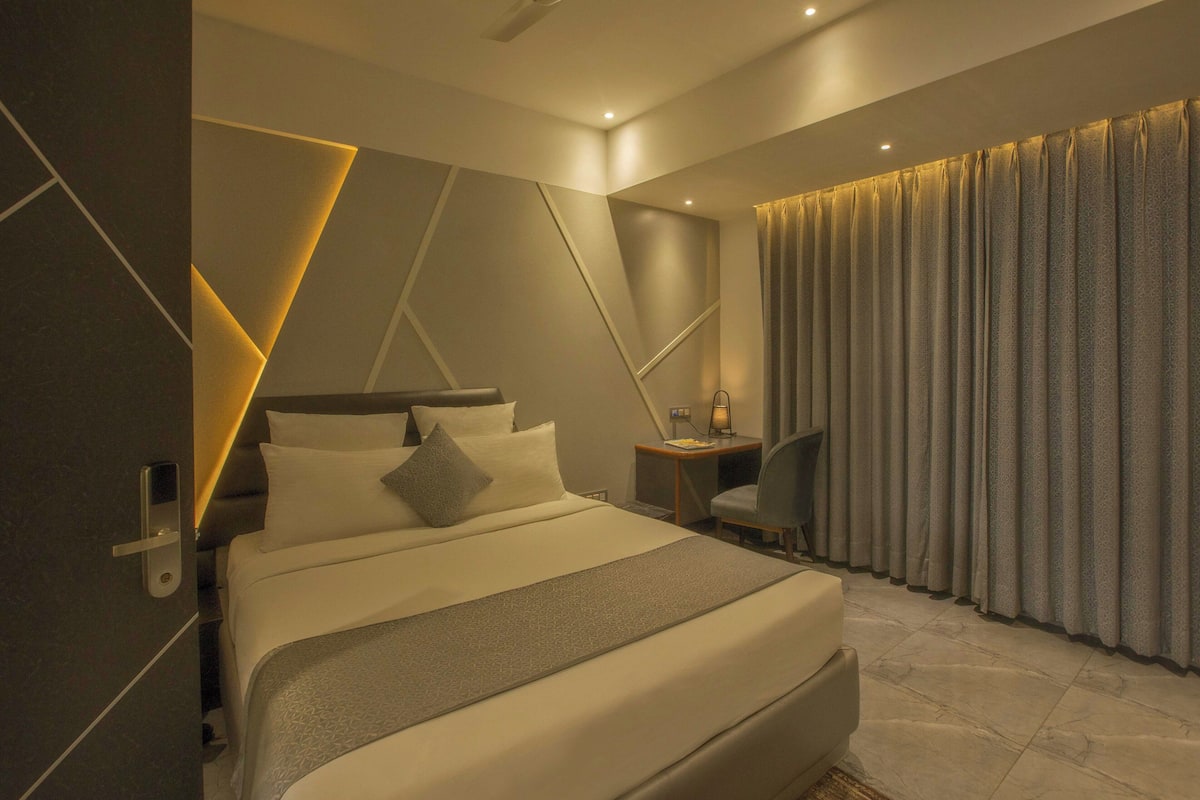 A modern hotel room with a large bed, a desk, and a curtain-covered window.