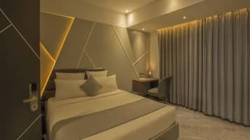 A modern hotel room with a large bed, a desk, and a curtain-covered window.