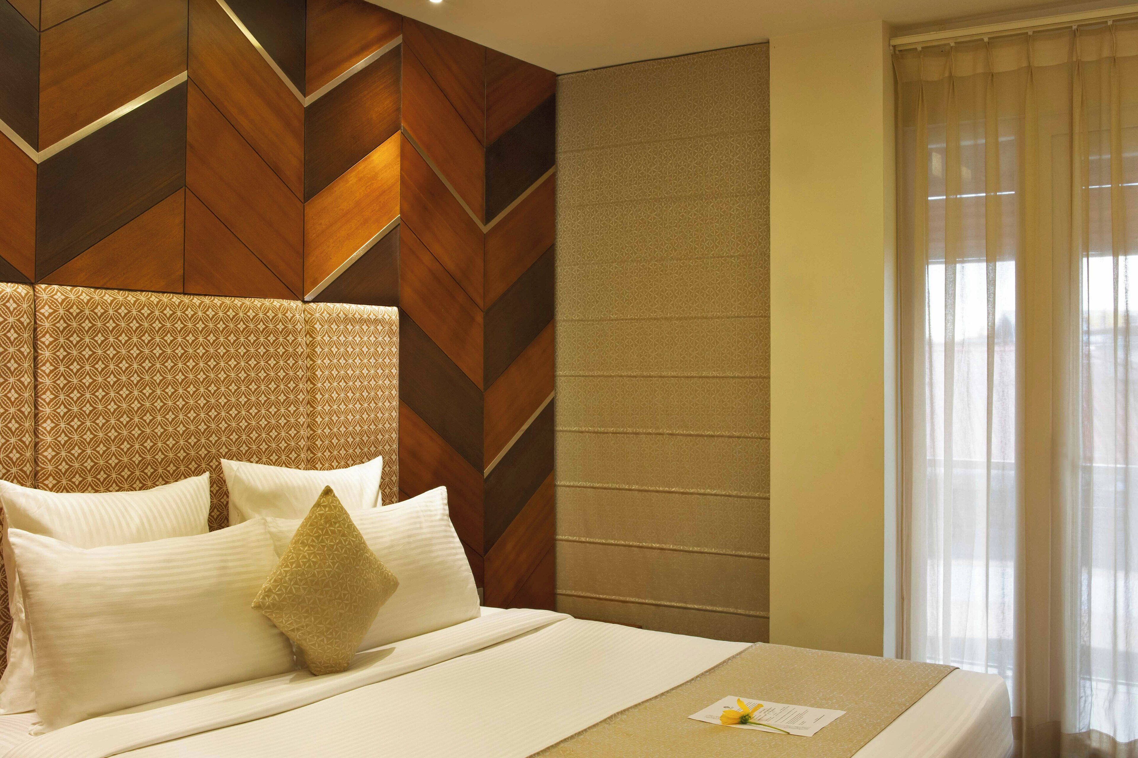 Una habitación de hotel con una cama grande, un cabecero estampado y una ventana con cortinas de gasa.