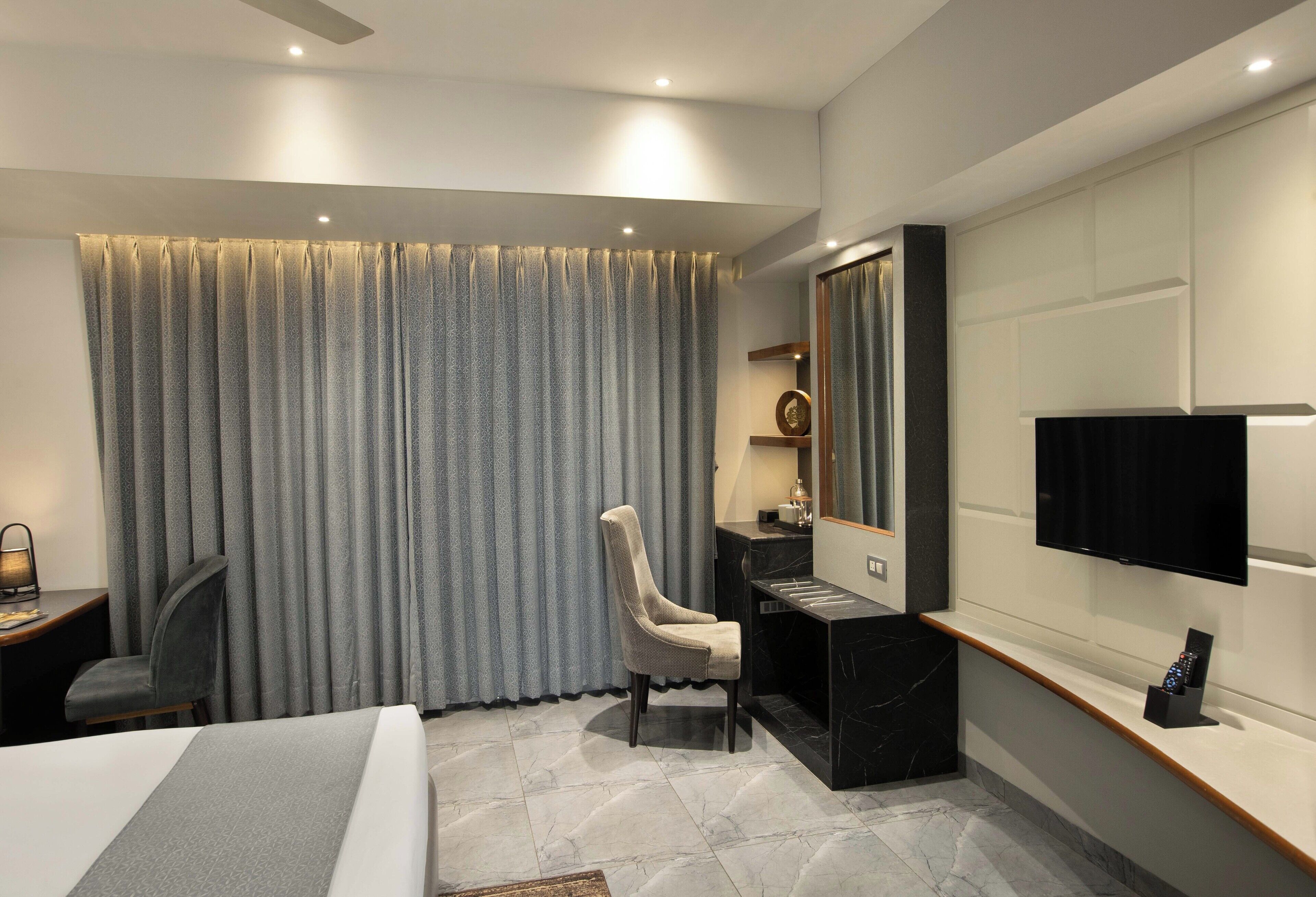 A modern hotel room with a bed, desk, chair, and a large mirror.