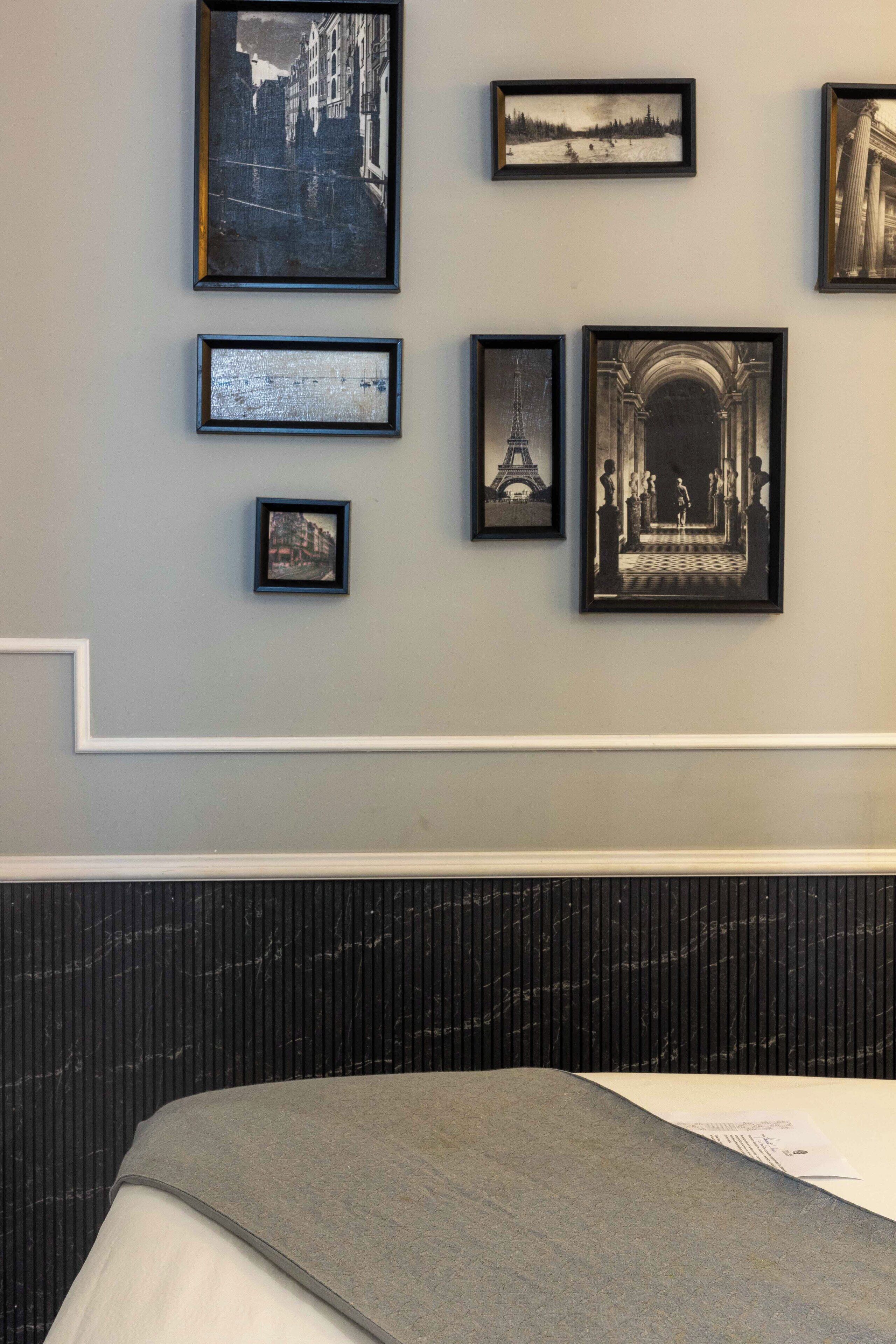 A hotel room with a bed, a marble bench, and a wall with framed pictures.