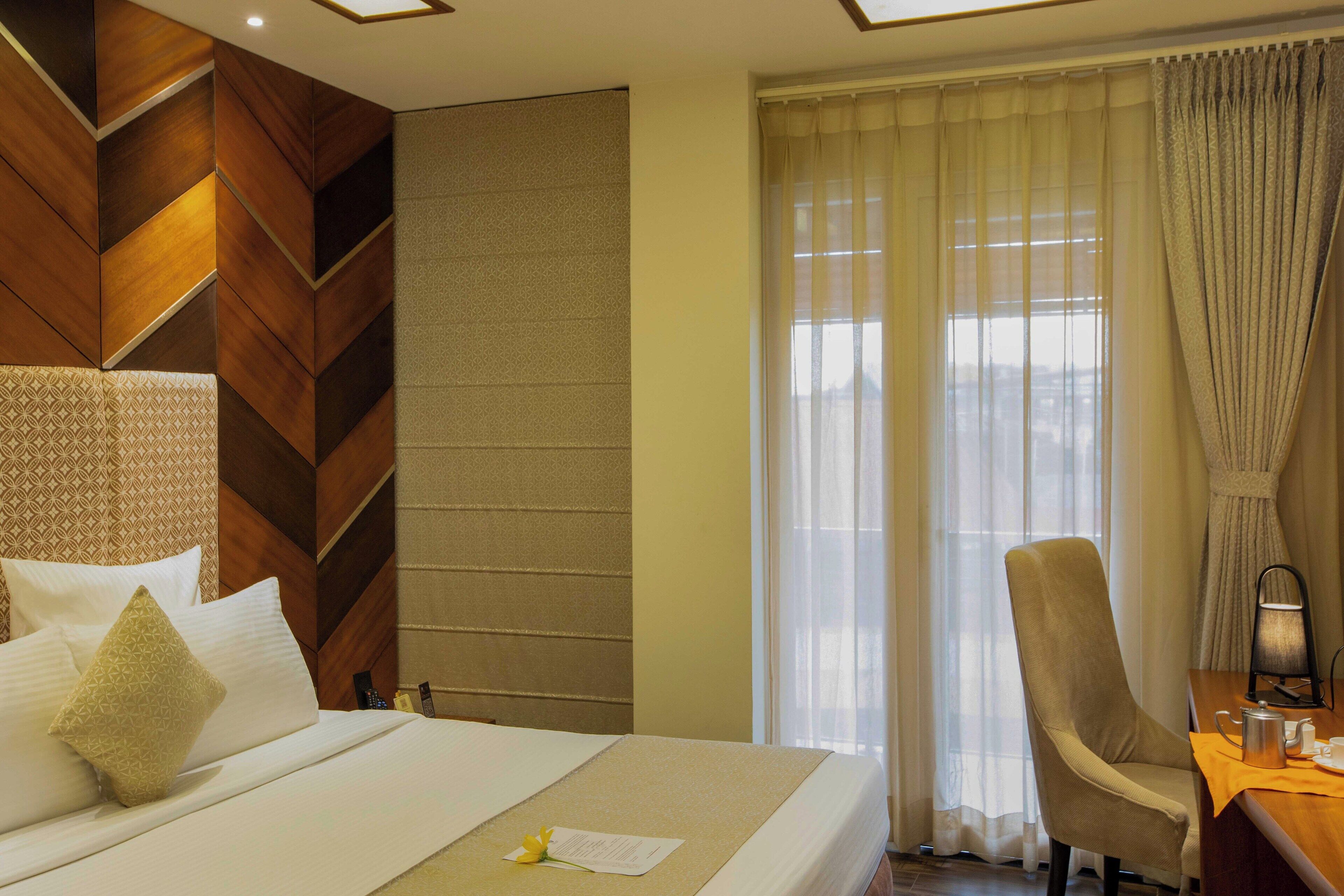 A hotel room with a bed, a desk, a chair, and a window with curtains.