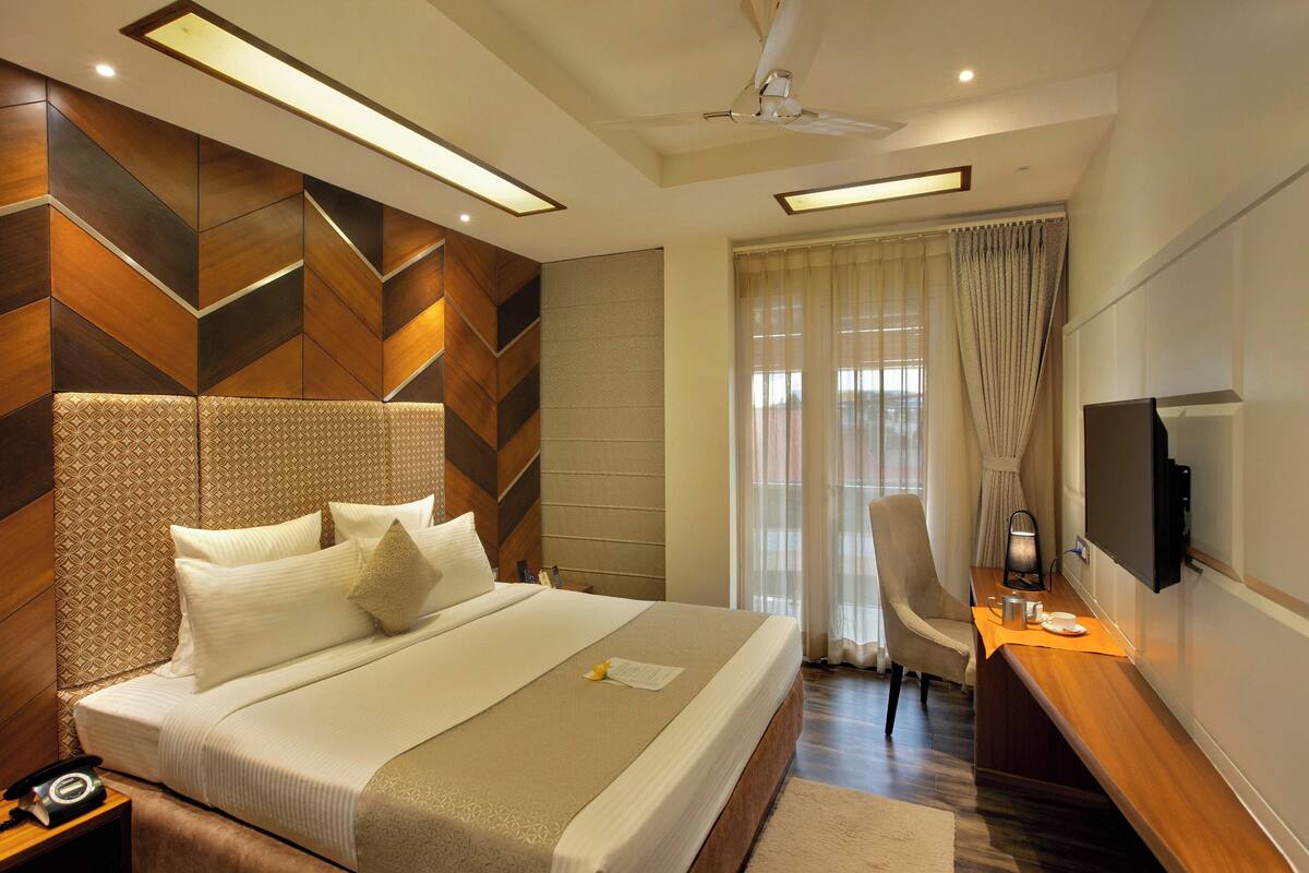 A modern hotel room with a large bed, a desk with a TV, and a ceiling fan.
