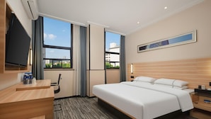A hotel room with a bed, bedside table, TV, and a view of buildings through large windows. - City Comfort Inn Huangshi Bei Station (Huangshi)