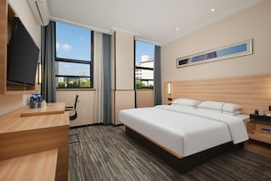 A hotel room with a bed, bedside table, TV, and a view of buildings through large windows. - City Comfort Inn Huangshi Bei Station (Huangshi)