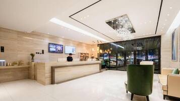 A modern hotel lobby with a reception desk, seating area, and a large window offering a view of the cityscape.
