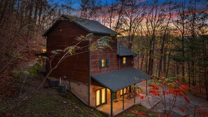 A rustic cabin with a stone foundation, a wooden exterior, and a porch with seating.