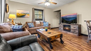 A living room with a sofa, coffee table, fireplace, TV, and a ceiling fan.