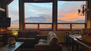 A cozy living room with a large window offering a mountain view. There is a sofa, a television, and a dining area with a table and chairs. - Beautiful Views! Home near Grand Canyon, Flagstaff (Flagstaff)