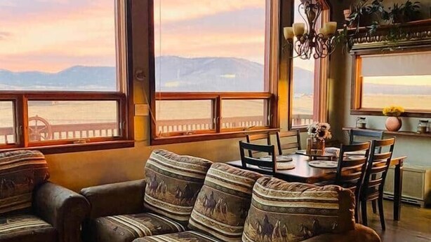 A cozy living room with a large sofa, a dining table, and chairs. There are large windows offering a view of the mountains. - Beautiful Views! Home near Grand Canyon, Flagstaff (Flagstaff)