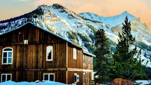 A rustic wooden building with a snow-covered landscape and mountains in the background. - Luxury Yellowstone Chalet - Mountain Views with Sauna! (Cooke City-Silver Gate)