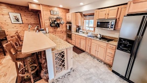 A kitchen with wooden cabinets, a granite countertop, and stainless steel appliances. - Luxury Yellowstone Chalet - Mountain Views with Sauna! (Cooke City-Silver Gate)