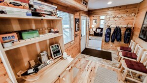 A cozy cabin interior with wooden walls and floors, a shelf with board games, a sign welcoming guests, and a seating area with cushions. - Luxury Yellowstone Chalet - Mountain Views with Sauna! (Cooke City-Silver Gate)