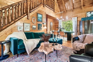 Un acogedor interior de cabaña de madera con una escalera de madera, un sofá color turquesa y un comedor.