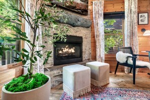 Una habitación acogedora con chimenea, suelo de madera y un amplio ventanal con cortinas.