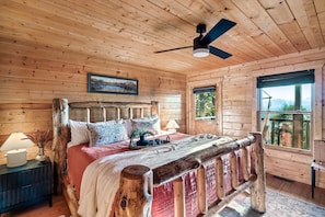 Un dormitorio de cabaña de madera con cama, mesita de noche y ventana.