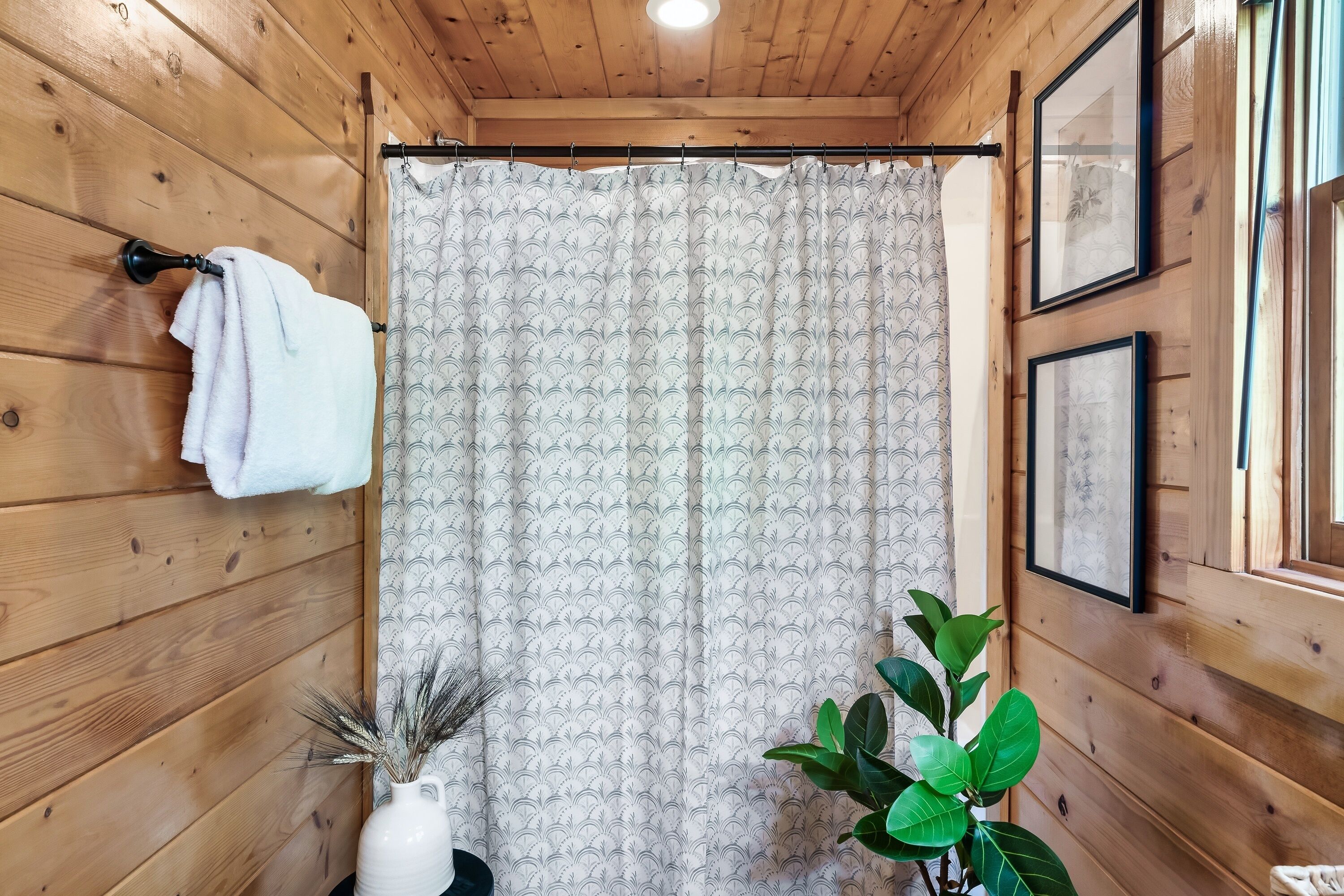 A wooden cabin bathroom with a shower curtain, a towel hanging on a hook, and framed pictures on the wall.