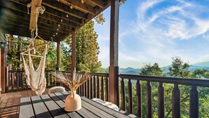 Una terraza de madera con una hamaca y un jarrón de plantas secas, con vistas a un paisaje montañoso.