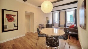 Un salon moderne avec une table à manger ronde, des chaises noires à motifs, un grand miroir, une œuvre d’art encadrée et un luminaire suspendu.