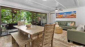 Un'ampia zona giorno con un tavolo da pranzo in legno, un divano verde e una grande finestra che si affaccia su un lussureggiante spazio verde.
