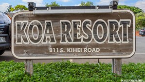 Un cartello in legno con la scritta "KOA RESORT 811 S. KIHEI ROAD" e una telecamera posizionata in alto.
