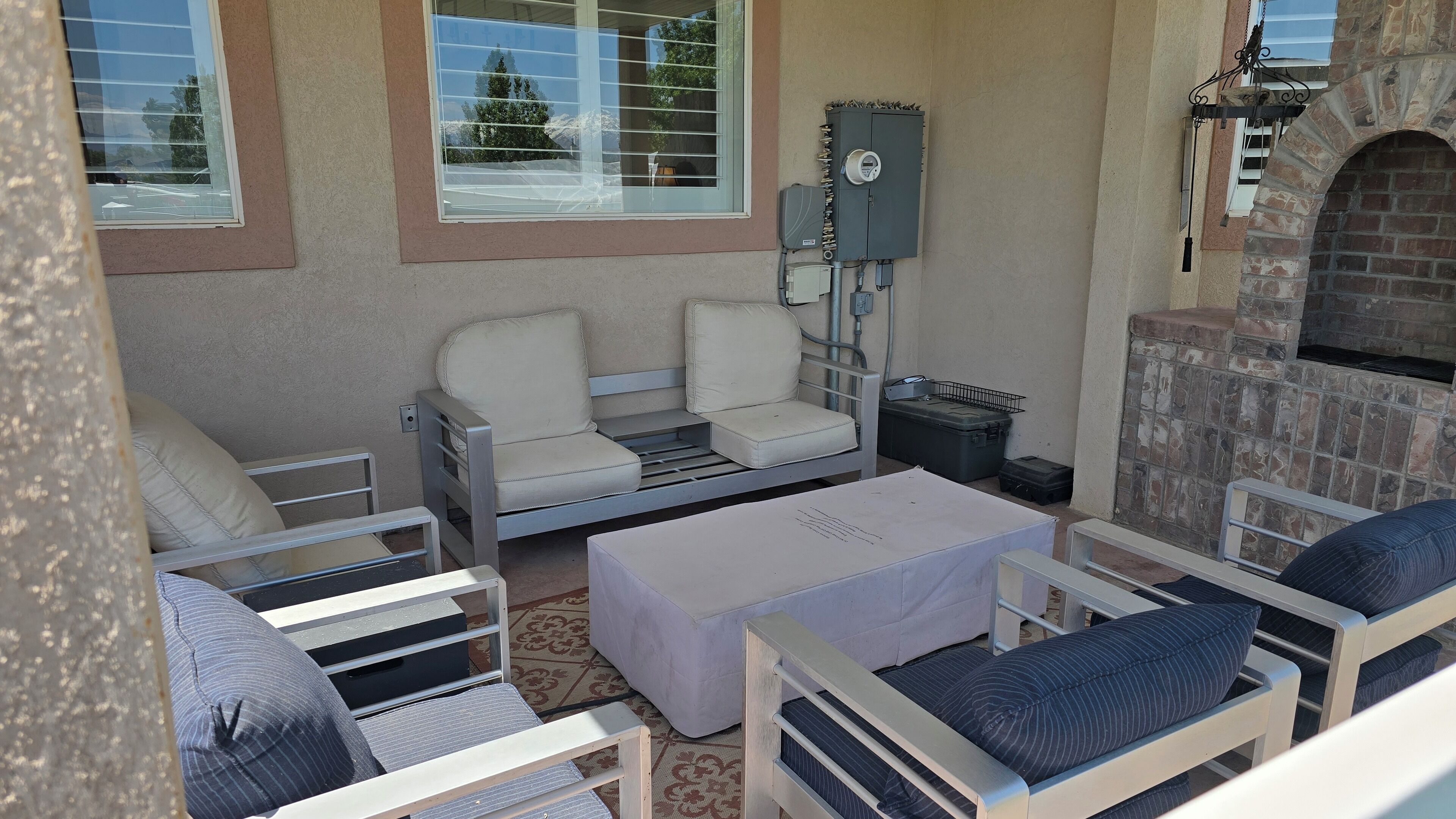 Een terras met twee witte loungestoelen, een kleine tafel en een vuurplaats van baksteen.