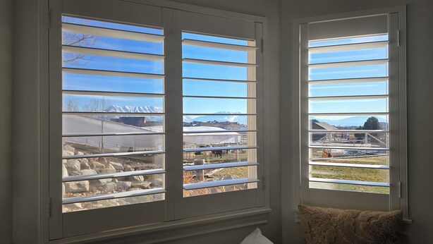 Habitación con dos ventanas que dan a una granja, con montañas al fondo.