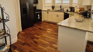 Una cocina con suelo de madera, armarios blancos, un refrigerador negro, un microondas y un lavamanos.