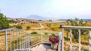 Una scala conduce a un balcone con vista su un paesaggio rurale, con campi, alcune case e montagne in lontananza.