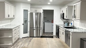 Una cucina con mobili bianchi, frigorifero in acciaio inossidabile, forno a microonde ed elettrodomestici.