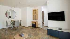 A modern living room with a dining area, a TV mounted on the wall, and a ceiling fan.