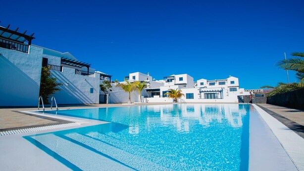 A modern hotel with a swimming pool, white buildings, and clear blue skies.