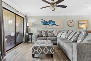 Ein Wohnzimmer mit grauem Sofa, gestreiftem Ottomanen und einem Deckenventilator.