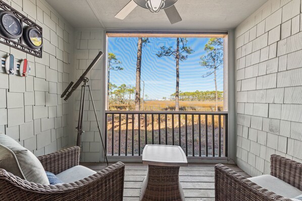 A balcony with wicker furniture, a telescope, and a view of trees and grass.