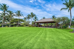 A well-maintained lawn with a gazebo, palm trees, and a clear sky.