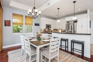 A modern kitchen with white cabinetry, stainless steel appliances, and a central island with bar stools.