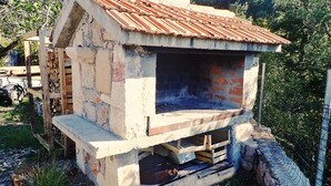 A rustic outdoor stone oven with a metal roof, surrounded by greenery. - Vacation home in traditional style in a very quiet location (Starigrad Paklenica)