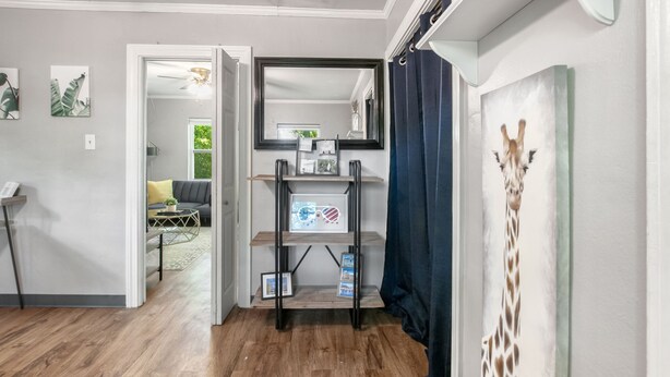 A hallway with a wooden floor, a mirror on the wall, a shelf with framed pictures, and a giraffe decoration.