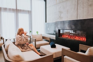 En kvinde slapper af i et moderne loungeområde med pejs, behagelige siddepladser og store vinduer.