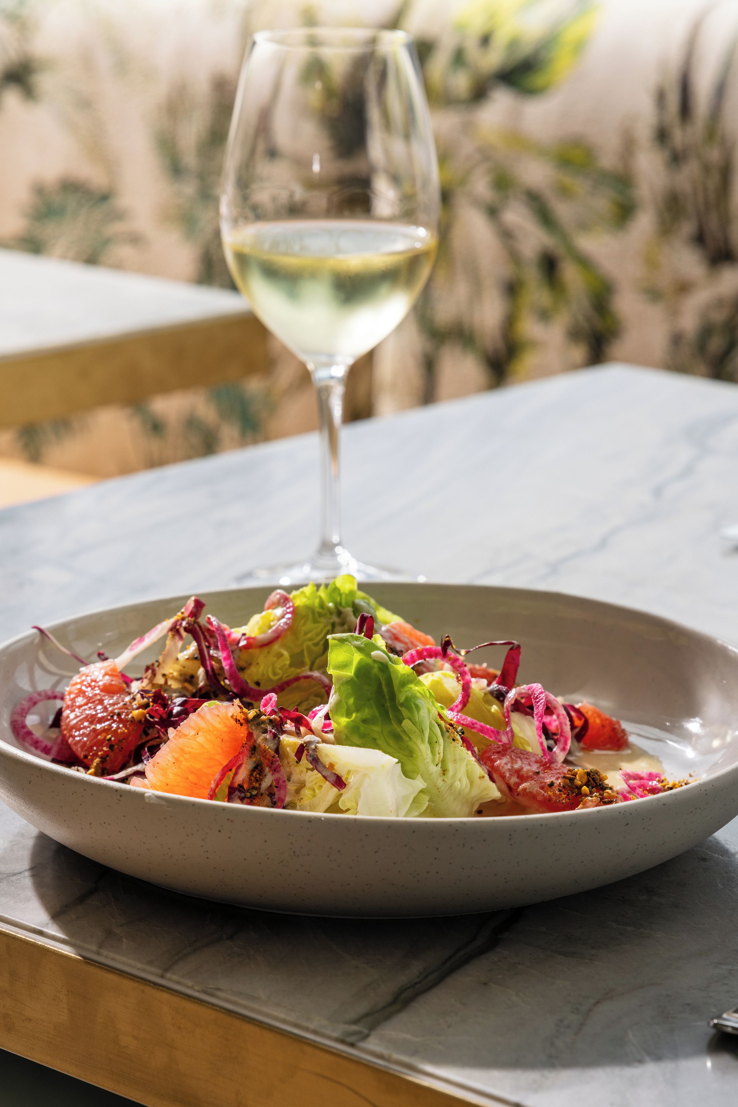 A plate of colorful salad with a glass of white wine on a table.