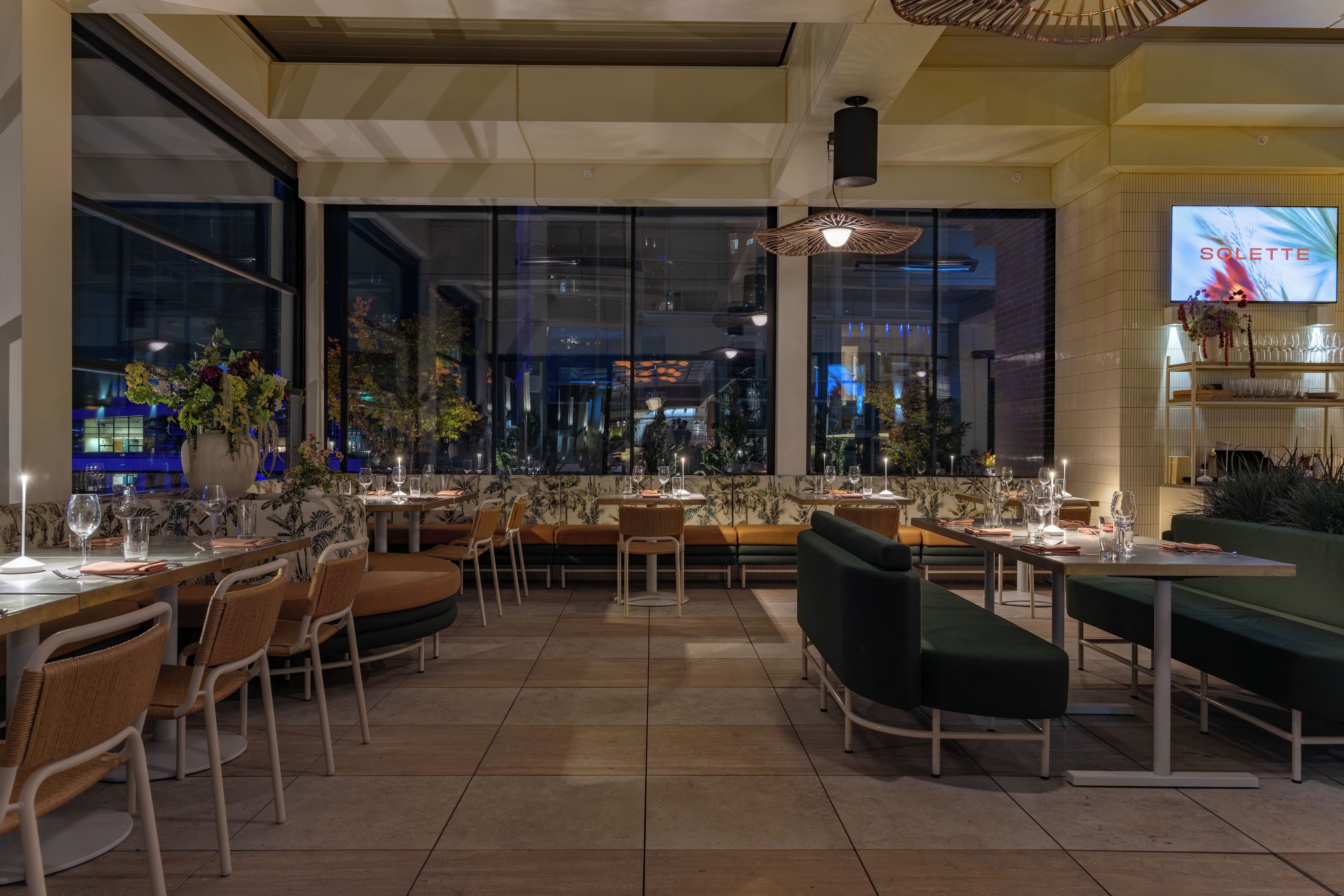Restaurante com várias mesas e cadeiras, amplas janelas e uma televisão exibindo 'SOLETTE'.